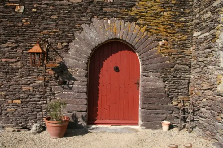 Porte en chêne peinte en rouge, posée dans une maçonnerie de schiste en plein cintre